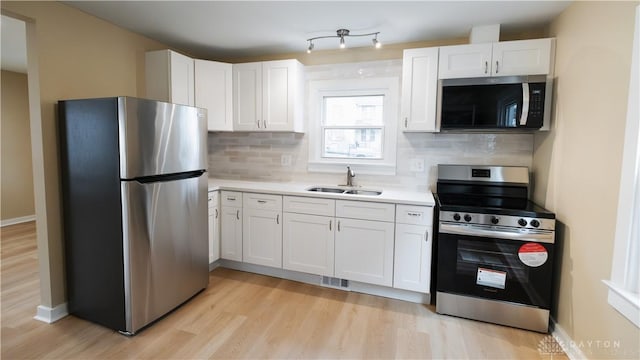 kitchen with stainless steel appliances, white cabinetry, sink, and light wood-type flooring