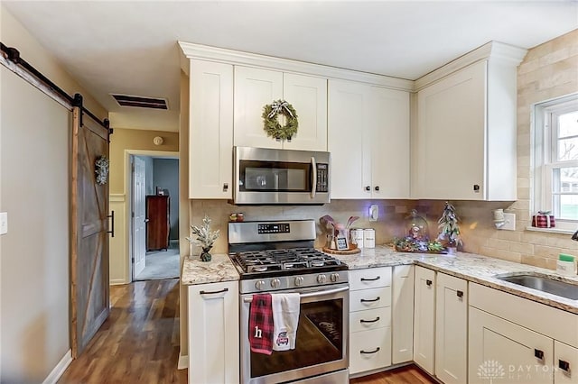 kitchen featuring appliances with stainless steel finishes, tasteful backsplash, light stone counters, wood-type flooring, and a barn door