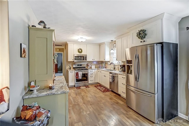 kitchen featuring sink, light stone countertops, appliances with stainless steel finishes, light hardwood / wood-style floors, and white cabinetry