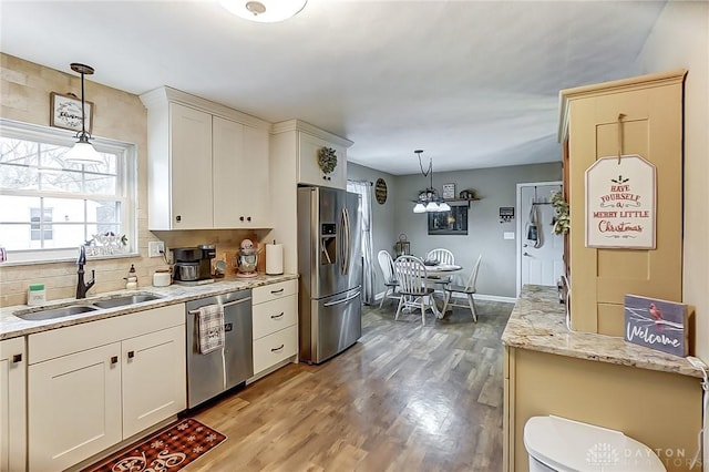 kitchen with sink, hanging light fixtures, light wood-type flooring, appliances with stainless steel finishes, and white cabinetry