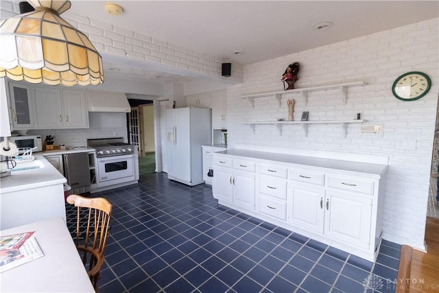 kitchen with tasteful backsplash, brick wall, premium range hood, white appliances, and white cabinets