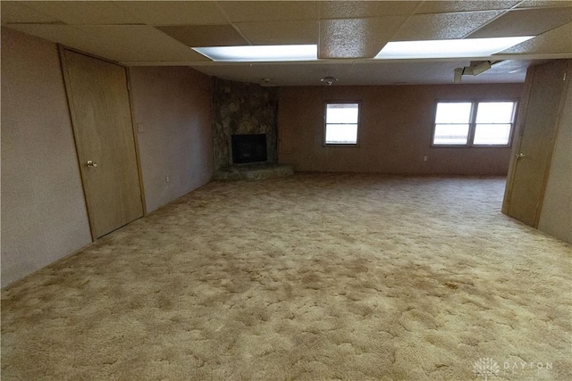 basement with a stone fireplace, a drop ceiling, and carpet