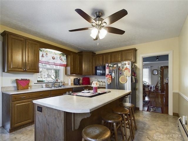 kitchen with a breakfast bar, ceiling fan, baseboard heating, sink, and a kitchen island