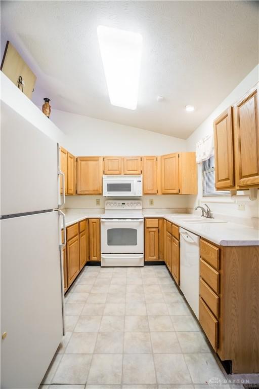 kitchen with light tile patterned floors, white appliances, vaulted ceiling, and sink