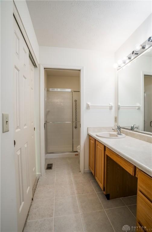 bathroom with tile patterned flooring, vanity, toilet, and a shower with shower door