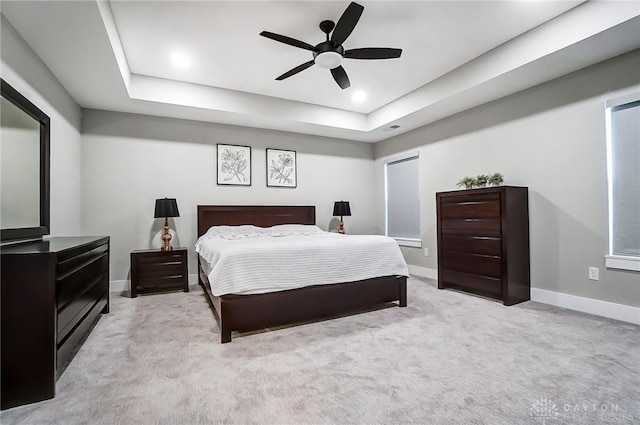 carpeted bedroom with a raised ceiling and ceiling fan