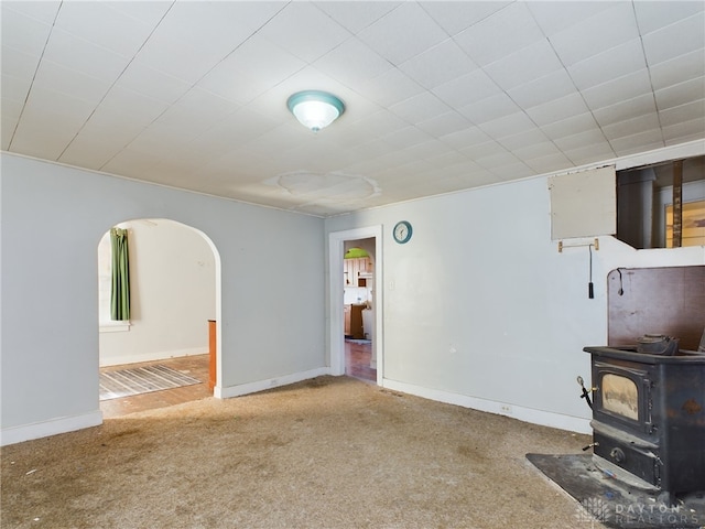 unfurnished living room with carpet floors, a wood stove, baseboards, and arched walkways