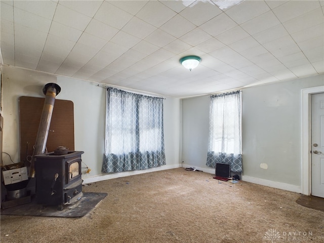 carpeted living area with a wood stove and baseboards