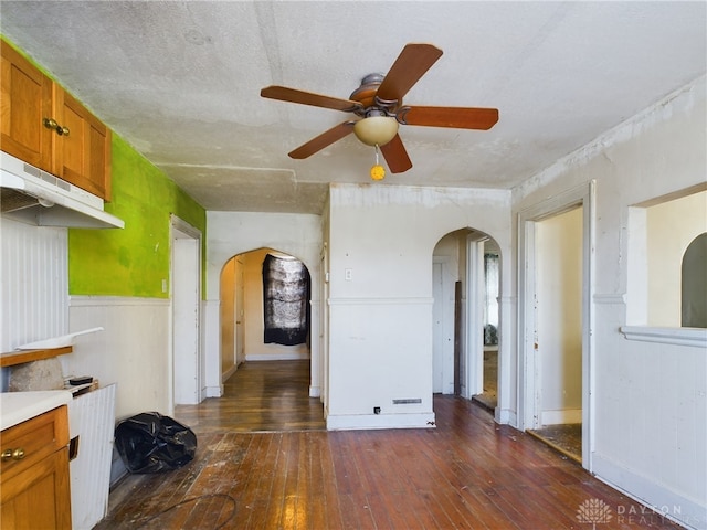 interior space featuring arched walkways, dark wood-type flooring, wainscoting, and a ceiling fan