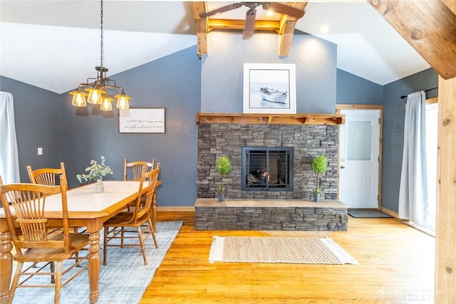 dining space with light wood-type flooring, lofted ceiling with beams, a chandelier, and a stone fireplace