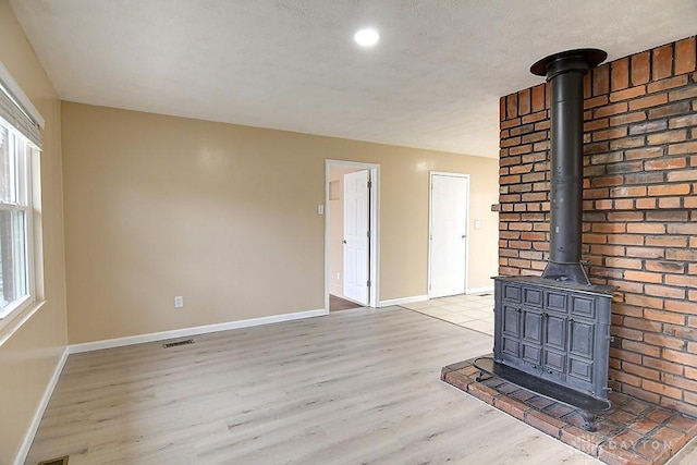 unfurnished living room featuring a wood stove, visible vents, baseboards, and wood finished floors