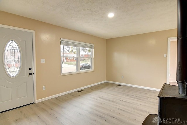 entrance foyer featuring visible vents, light wood-style floors, a wood stove, a textured ceiling, and baseboards