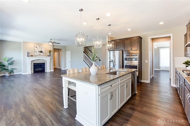 kitchen featuring a tile fireplace, sink, an island with sink, pendant lighting, and appliances with stainless steel finishes