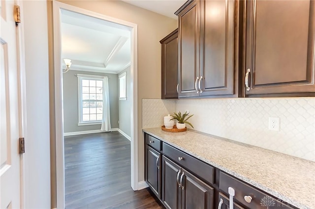 kitchen with backsplash, light stone counters, dark brown cabinetry, and dark wood-type flooring