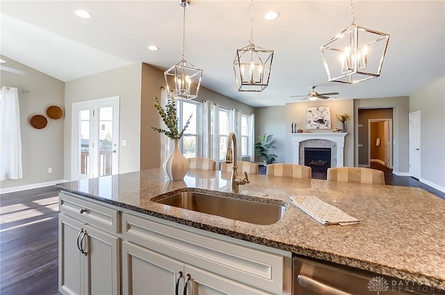 kitchen with stone counters, sink, dark hardwood / wood-style flooring, stainless steel dishwasher, and a tiled fireplace