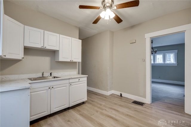 kitchen featuring white cabinetry, sink, ceiling fan with notable chandelier, and light hardwood / wood-style flooring