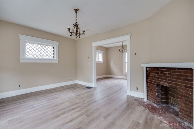 unfurnished living room with light wood-type flooring, a brick fireplace, plenty of natural light, and a notable chandelier