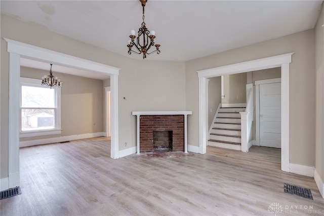 unfurnished living room with a fireplace, an inviting chandelier, and light hardwood / wood-style flooring