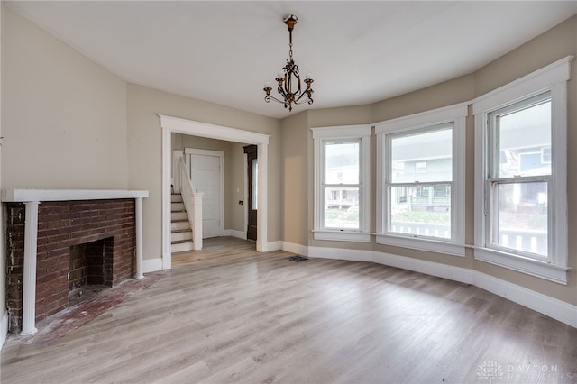 unfurnished living room featuring a chandelier, light hardwood / wood-style floors, and a brick fireplace