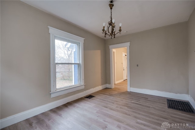 empty room with a notable chandelier and light wood-type flooring