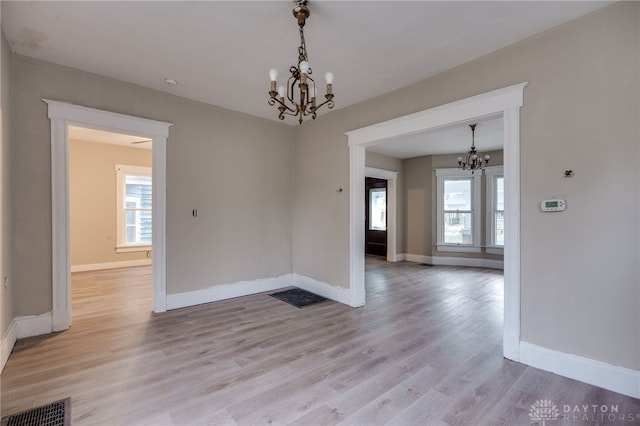 unfurnished dining area with light wood-type flooring, a healthy amount of sunlight, and a notable chandelier