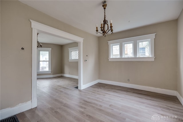 unfurnished room with a chandelier, light hardwood / wood-style flooring, and a healthy amount of sunlight