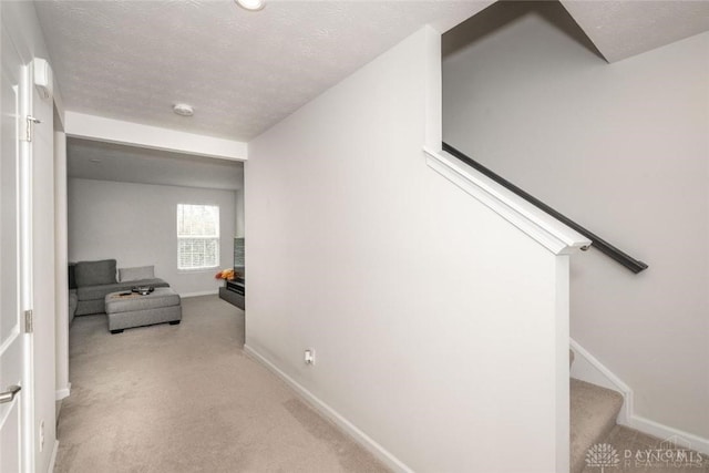 hallway featuring light colored carpet and a textured ceiling