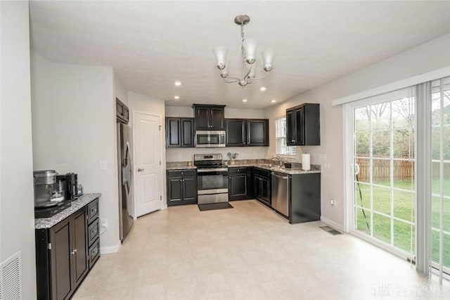 kitchen featuring pendant lighting, an inviting chandelier, sink, appliances with stainless steel finishes, and light stone counters