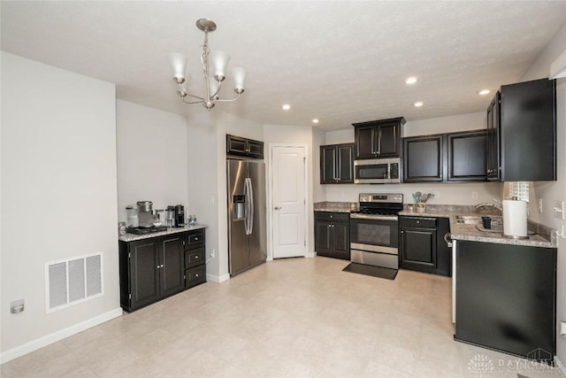 kitchen with light stone countertops, sink, stainless steel appliances, a notable chandelier, and decorative light fixtures