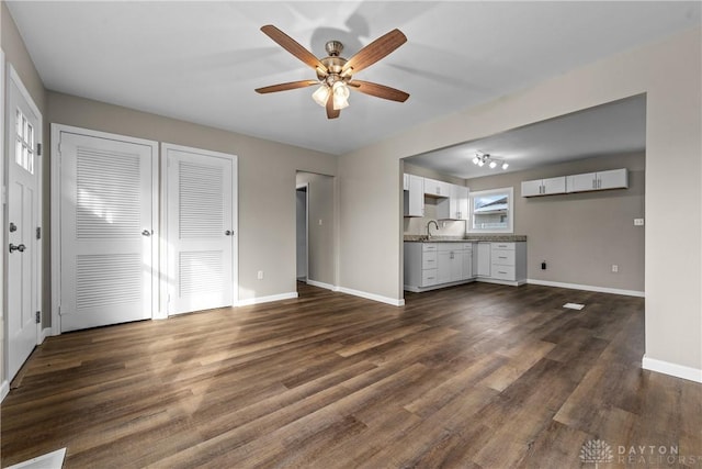 unfurnished living room with ceiling fan, sink, and dark wood-type flooring