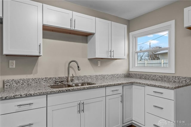 kitchen featuring light stone counters, white cabinetry, and sink