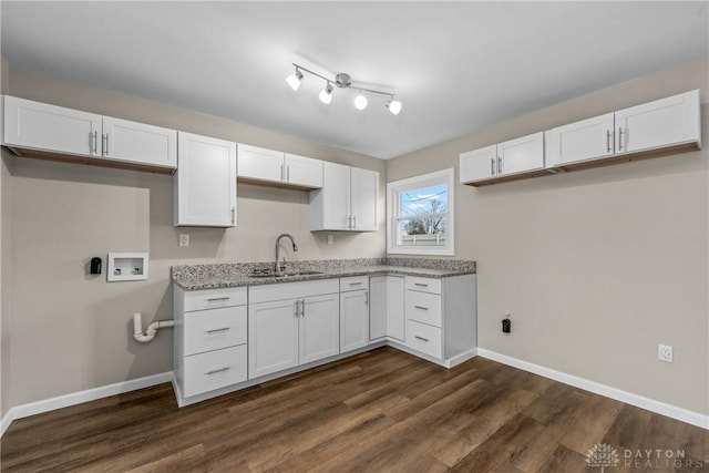 kitchen with light stone countertops, white cabinetry, dark wood-type flooring, and sink