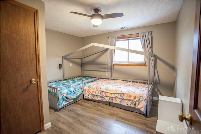 bedroom with ceiling fan, wood-type flooring, and a textured ceiling