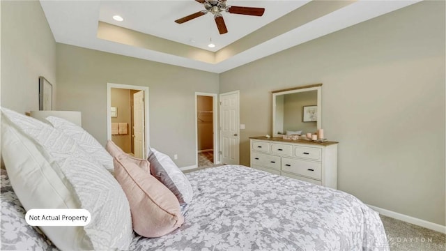 bedroom with ceiling fan, a tray ceiling, a walk in closet, a closet, and carpet