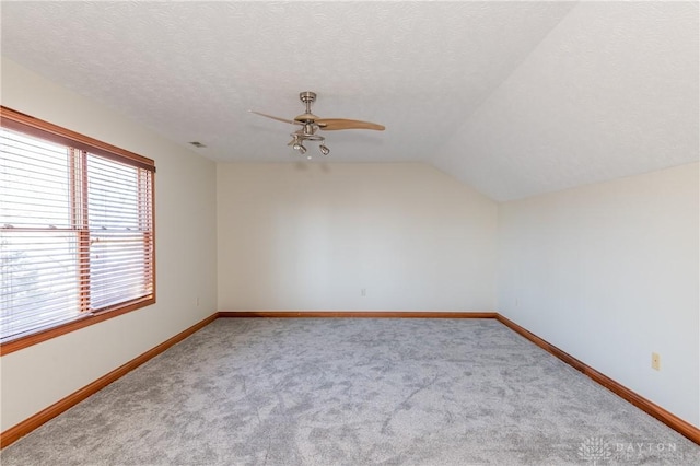 carpeted empty room with ceiling fan, a textured ceiling, and vaulted ceiling