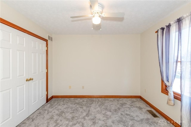 unfurnished bedroom featuring ceiling fan, light colored carpet, a textured ceiling, and a closet