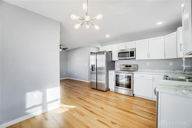 kitchen featuring appliances with stainless steel finishes, decorative light fixtures, white cabinetry, sink, and light hardwood / wood-style flooring