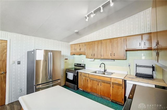 kitchen with vaulted ceiling, light countertops, a sink, appliances with stainless steel finishes, and brown cabinetry