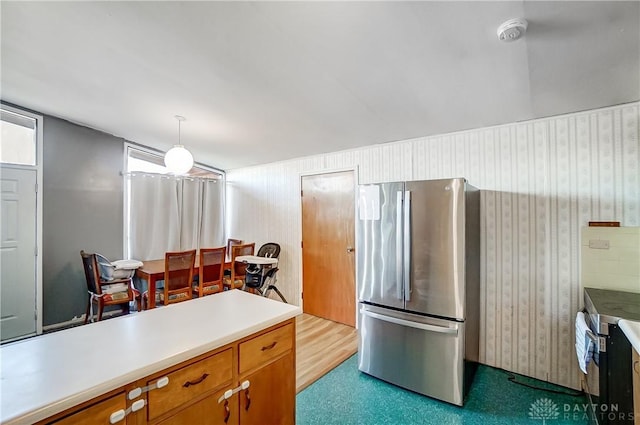 kitchen with freestanding refrigerator, light countertops, brown cabinetry, and pendant lighting