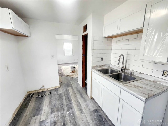 kitchen featuring light wood-style flooring, a sink, white cabinets, light countertops, and tasteful backsplash