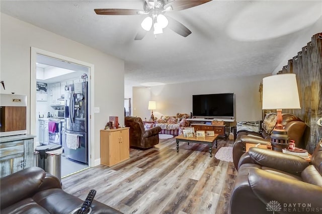 living room featuring ceiling fan, light hardwood / wood-style floors, and a textured ceiling