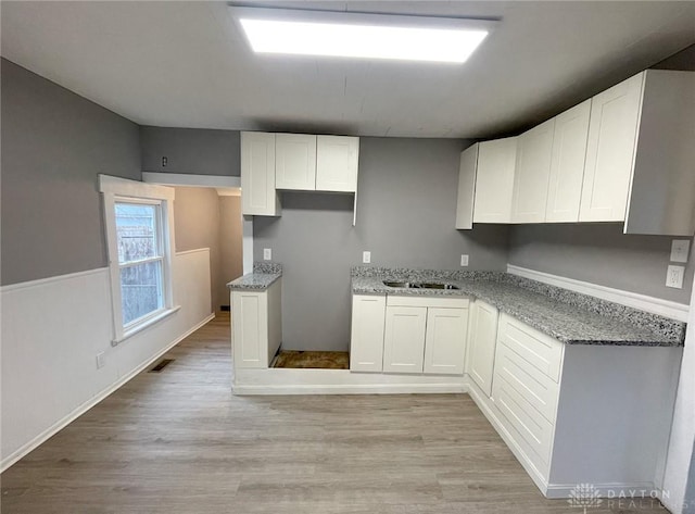 kitchen with light stone countertops, white cabinetry, sink, and light hardwood / wood-style floors