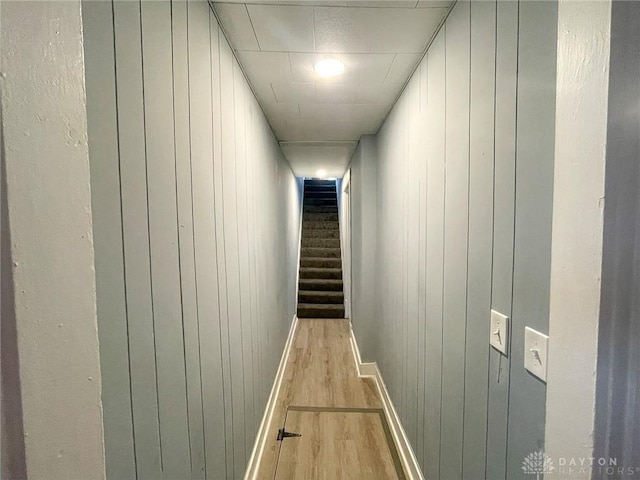 corridor with light hardwood / wood-style floors and wooden walls