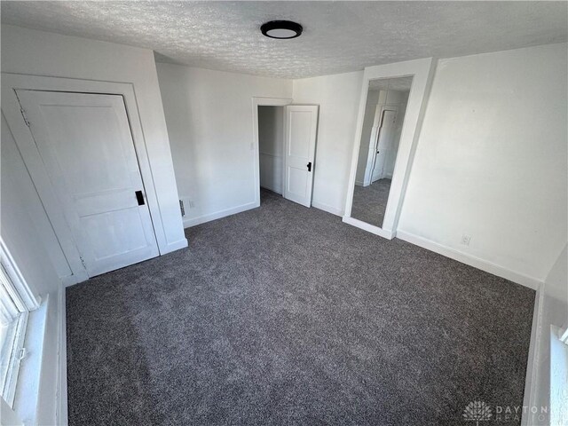 unfurnished bedroom with a closet, a textured ceiling, and dark colored carpet