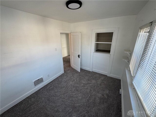 unfurnished room with built in features and dark carpet