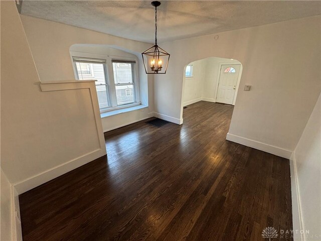 unfurnished dining area featuring dark hardwood / wood-style floors, an inviting chandelier, and a textured ceiling