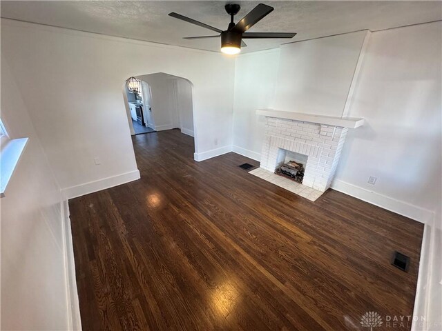 unfurnished living room with ceiling fan, a textured ceiling, a fireplace, and dark hardwood / wood-style flooring