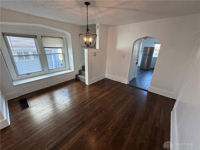 unfurnished dining area featuring dark wood-type flooring, a textured ceiling, and a chandelier