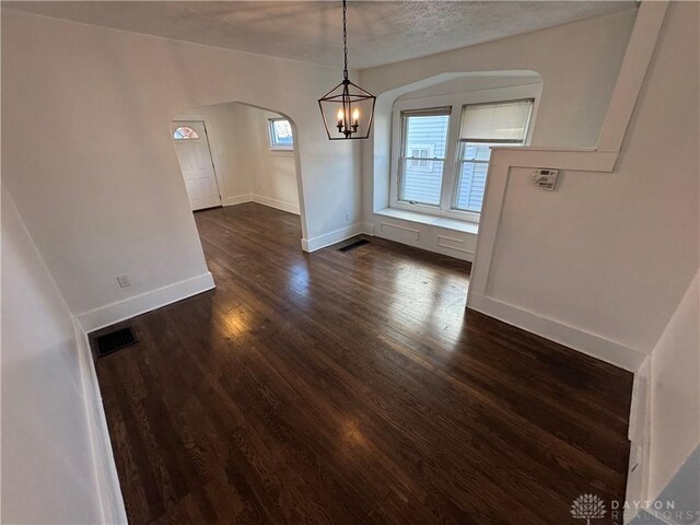 unfurnished dining area featuring dark hardwood / wood-style floors, a chandelier, and a textured ceiling