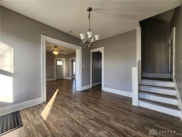 unfurnished dining area with ceiling fan with notable chandelier, plenty of natural light, and dark wood-type flooring